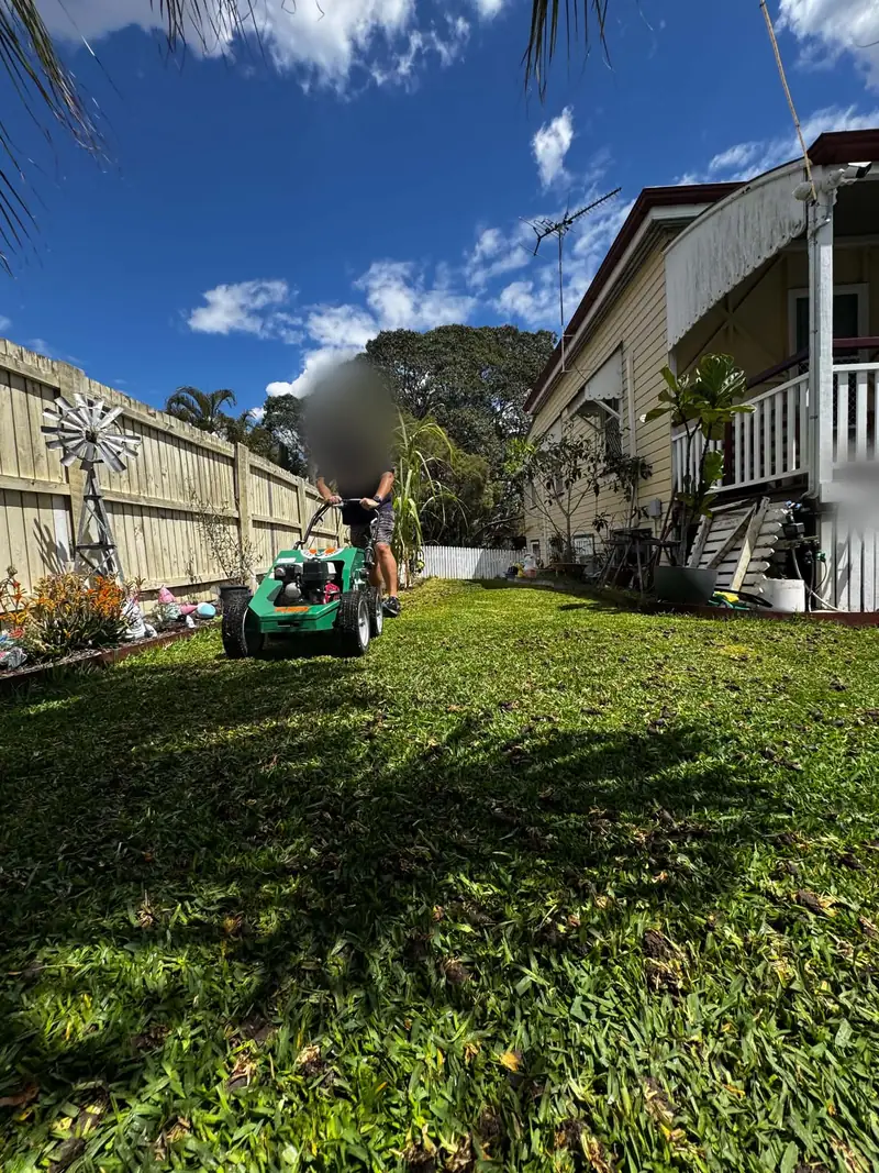 Person with a blurred face pushing a hired Billy Goat core aerator across a Sir Walter Buffalo lawn