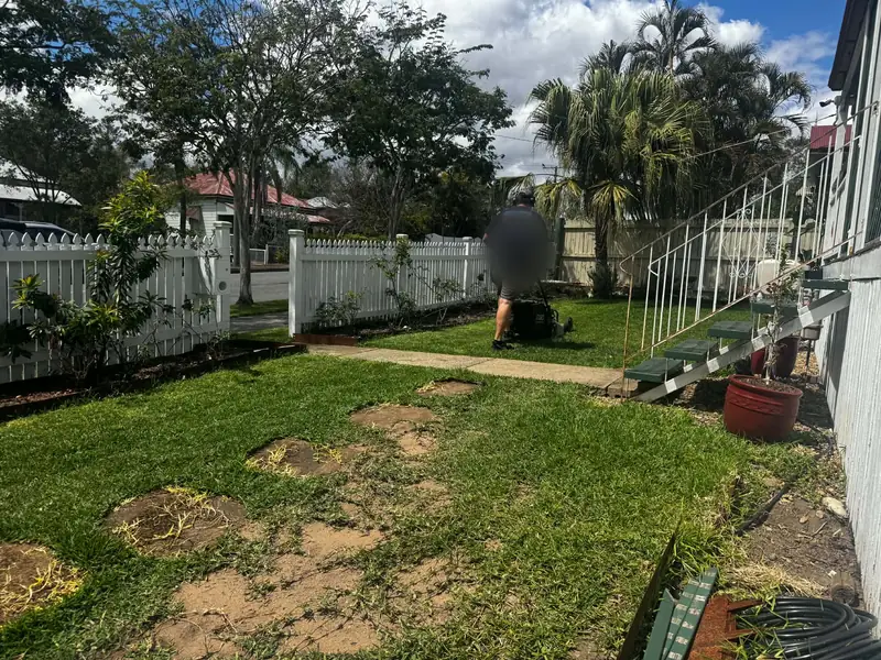 Person with a blurred face mowing over aeration cores on a front lawn with patches of bare clay